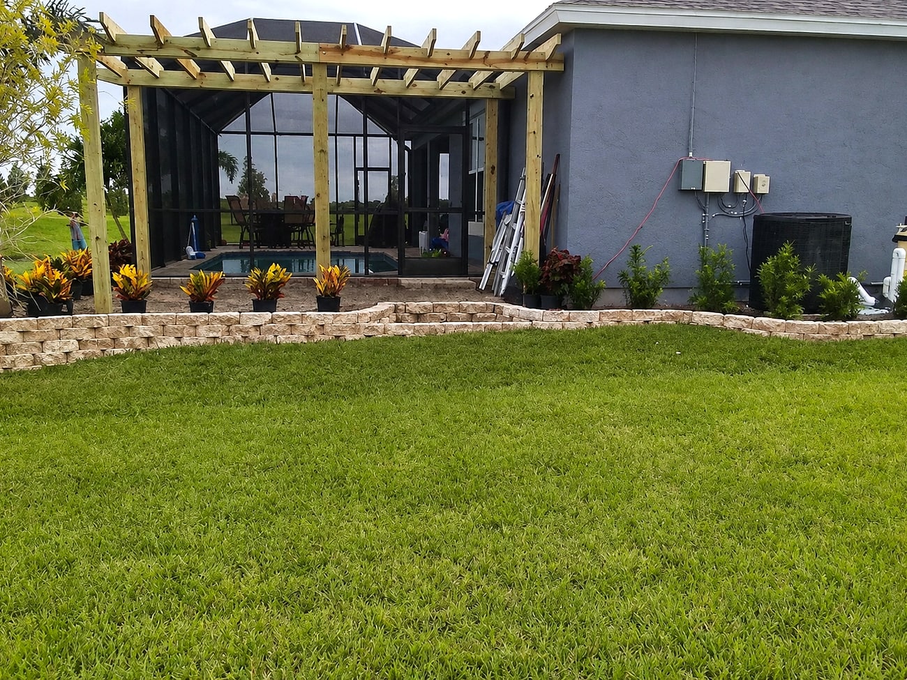 A curved paver retaining wall along a lawn near a pergola and screened pool enclosure, built by Premier Lawn Care