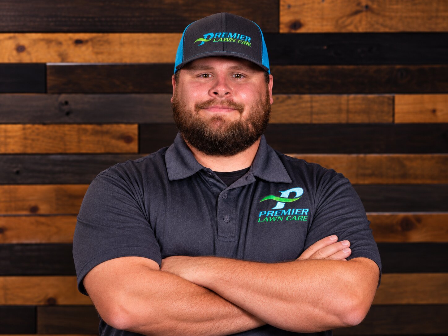 Aaron Herring, Operations Manager at Premier Lawn Care, wearing a branded cap with his arms crossed