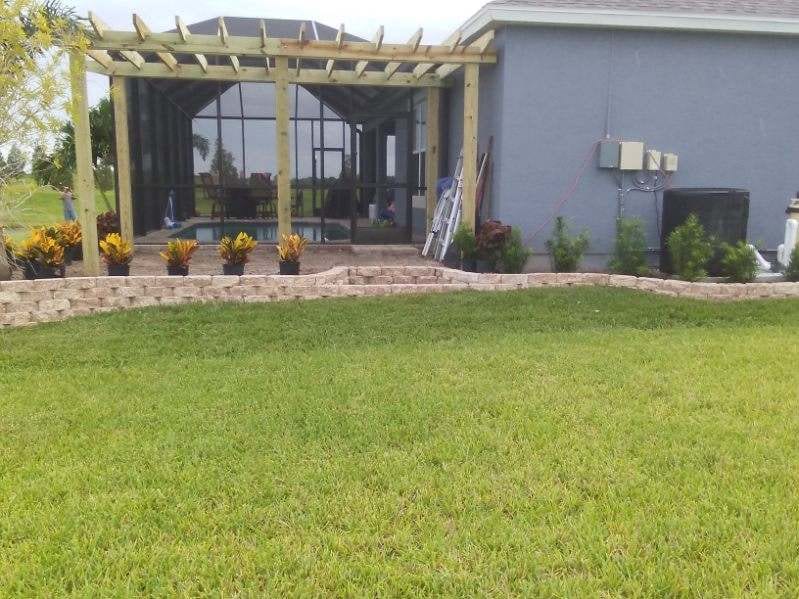 A curved paver retaining wall along a lawn near a pergola and screened pool enclosure