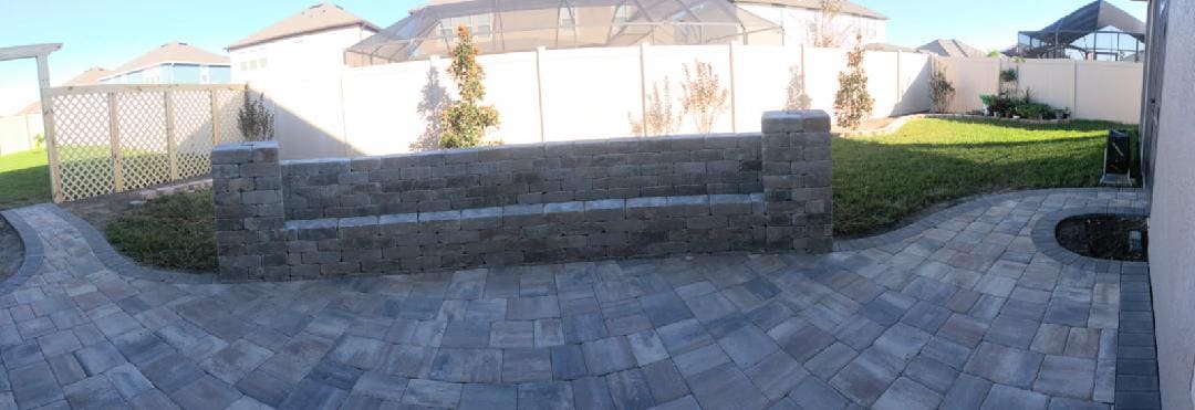 A paver patio with a stacked-stone seat wall along a screened backyard