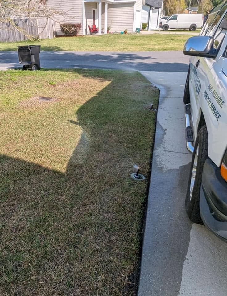Sprinkler heads along a lawn edge beside a parked service truck on a driveway