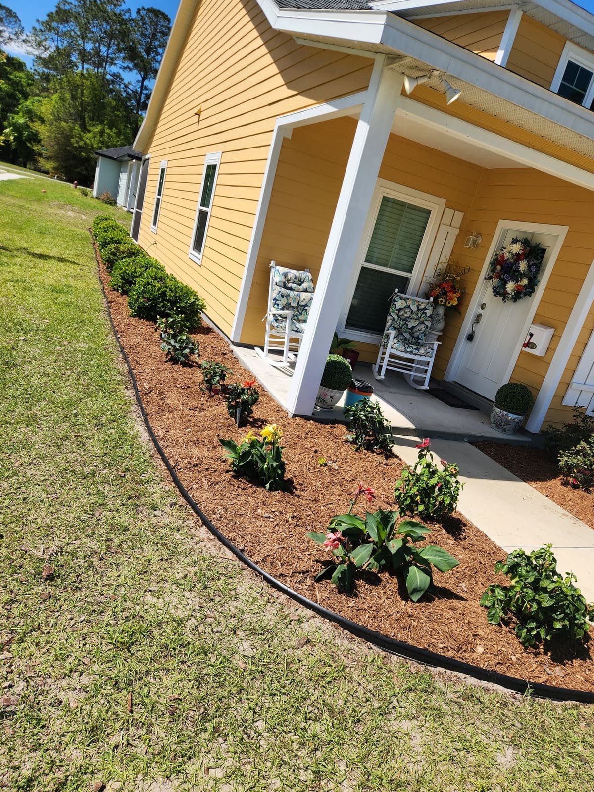 A curved planting bed with tropical flowers and shrubs along a covered front porch