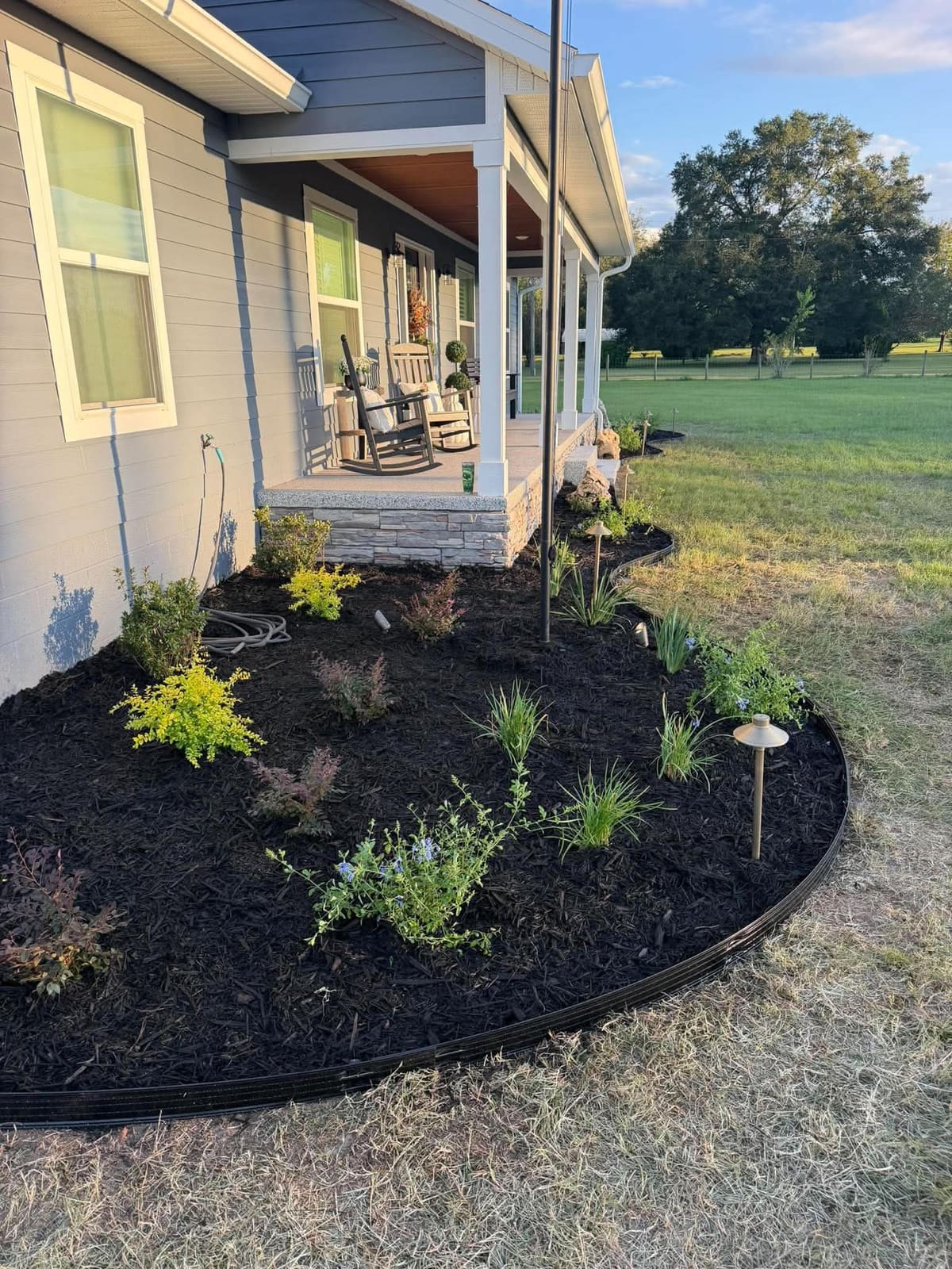 A freshly mulched curved planting bed with new plantings and landscape lighting on a rural property