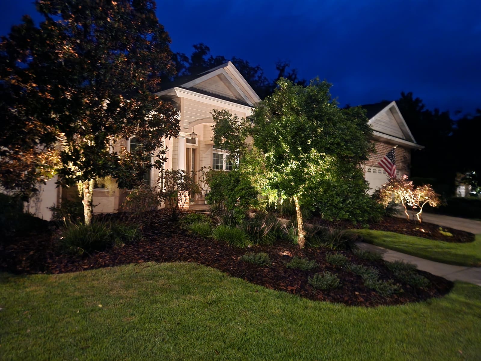A house facade with landscape lighting and planting beds at dusk