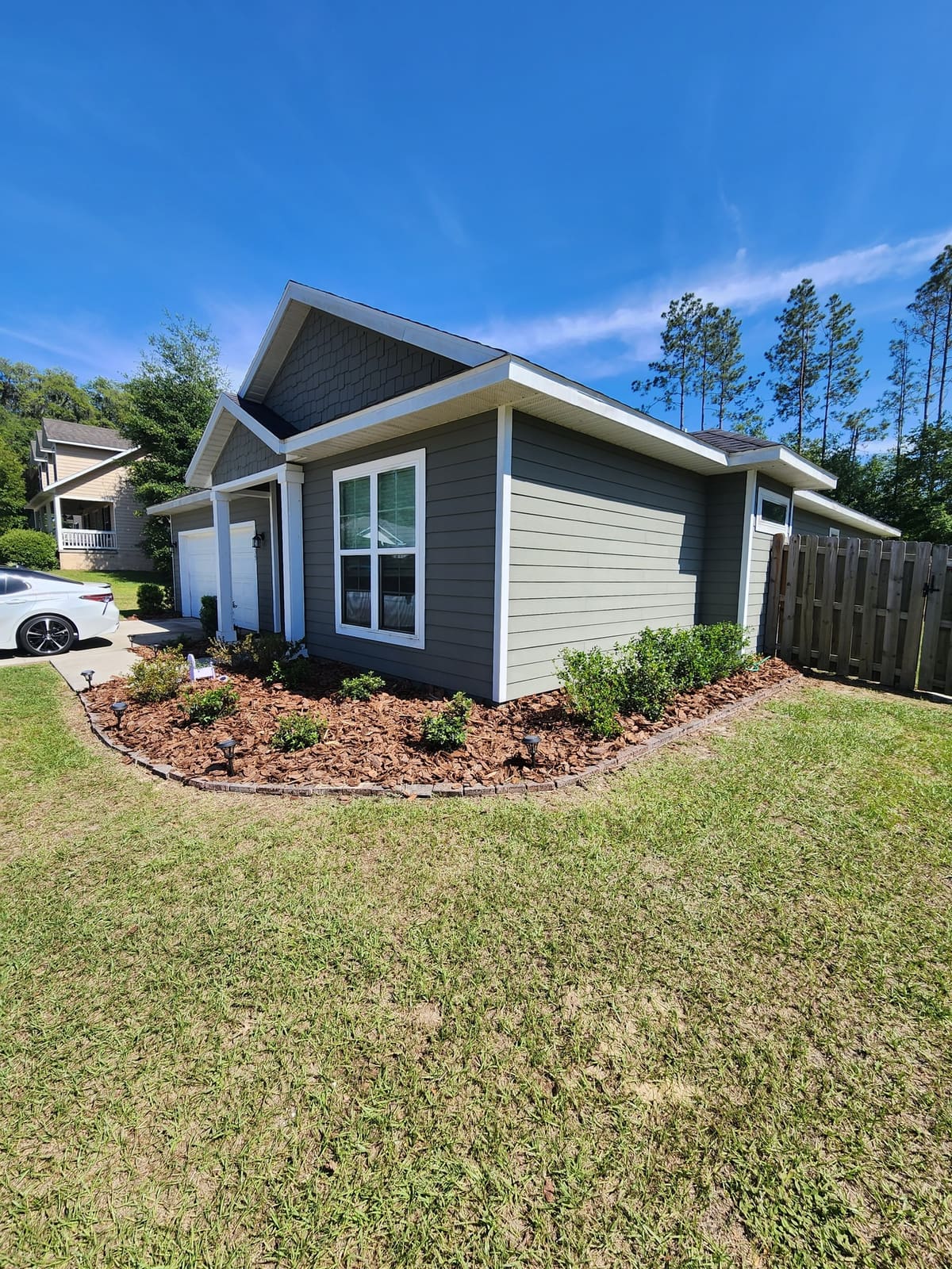 A new mulch planting bed with shrubs along the foundation of a gray house