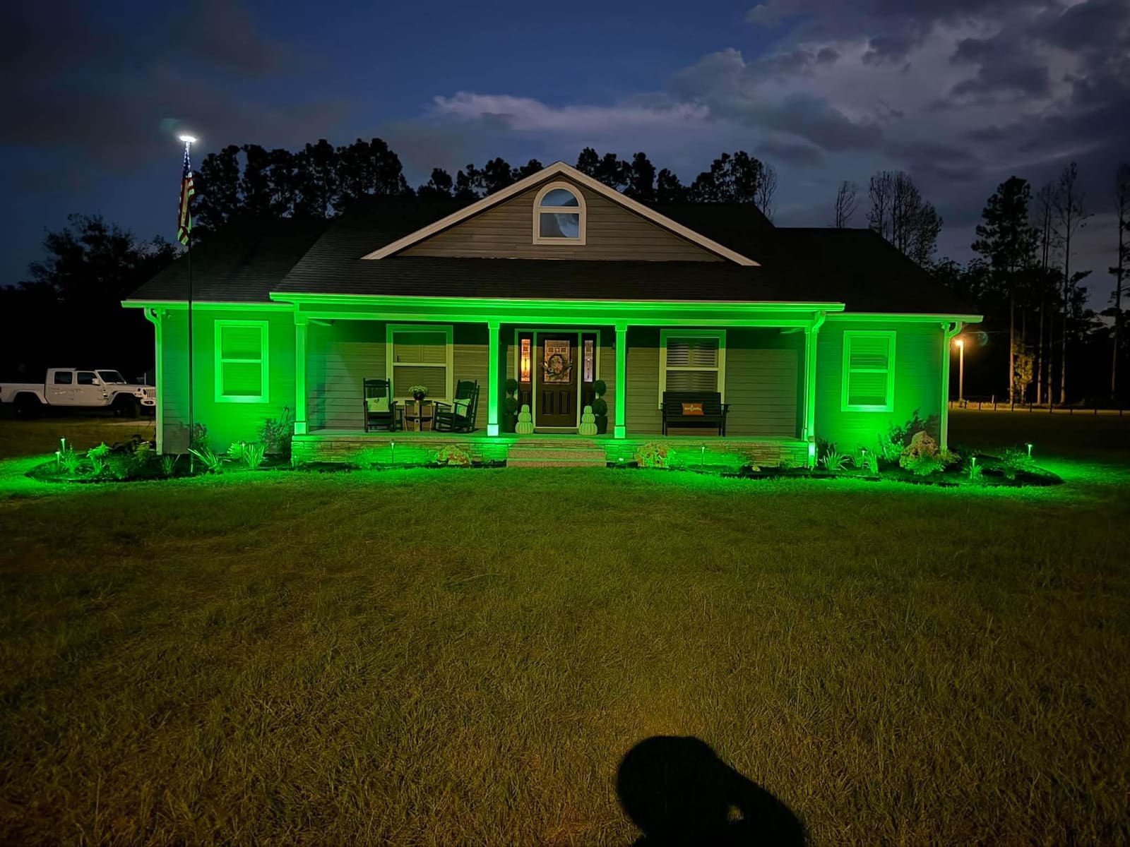 A farmhouse-style home with green landscape lighting along the porch and roofline at night