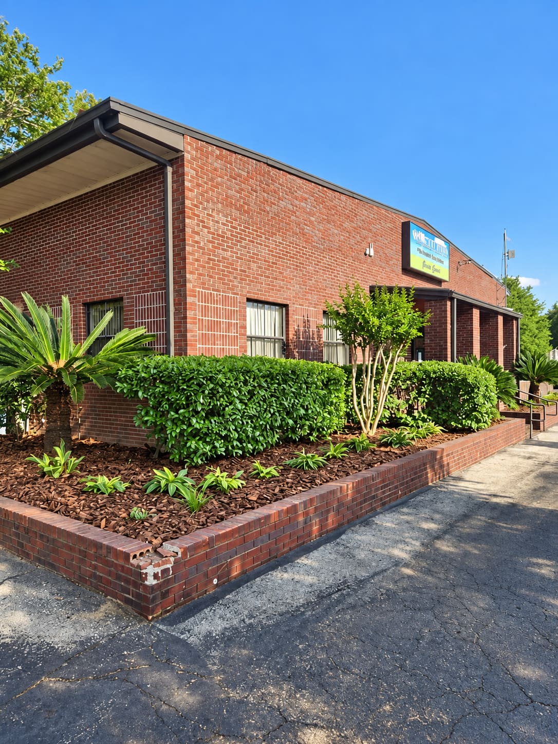 A trimmed hedge and planting bed along a brick commercial building