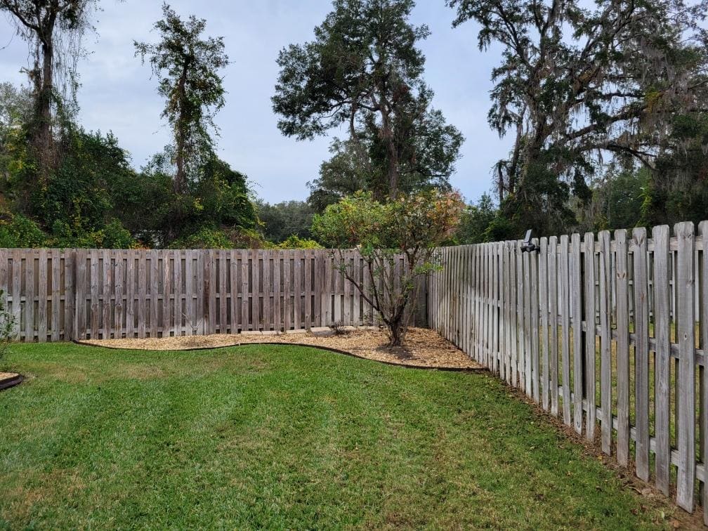 A mulch planting bed in a backyard corner along a fence