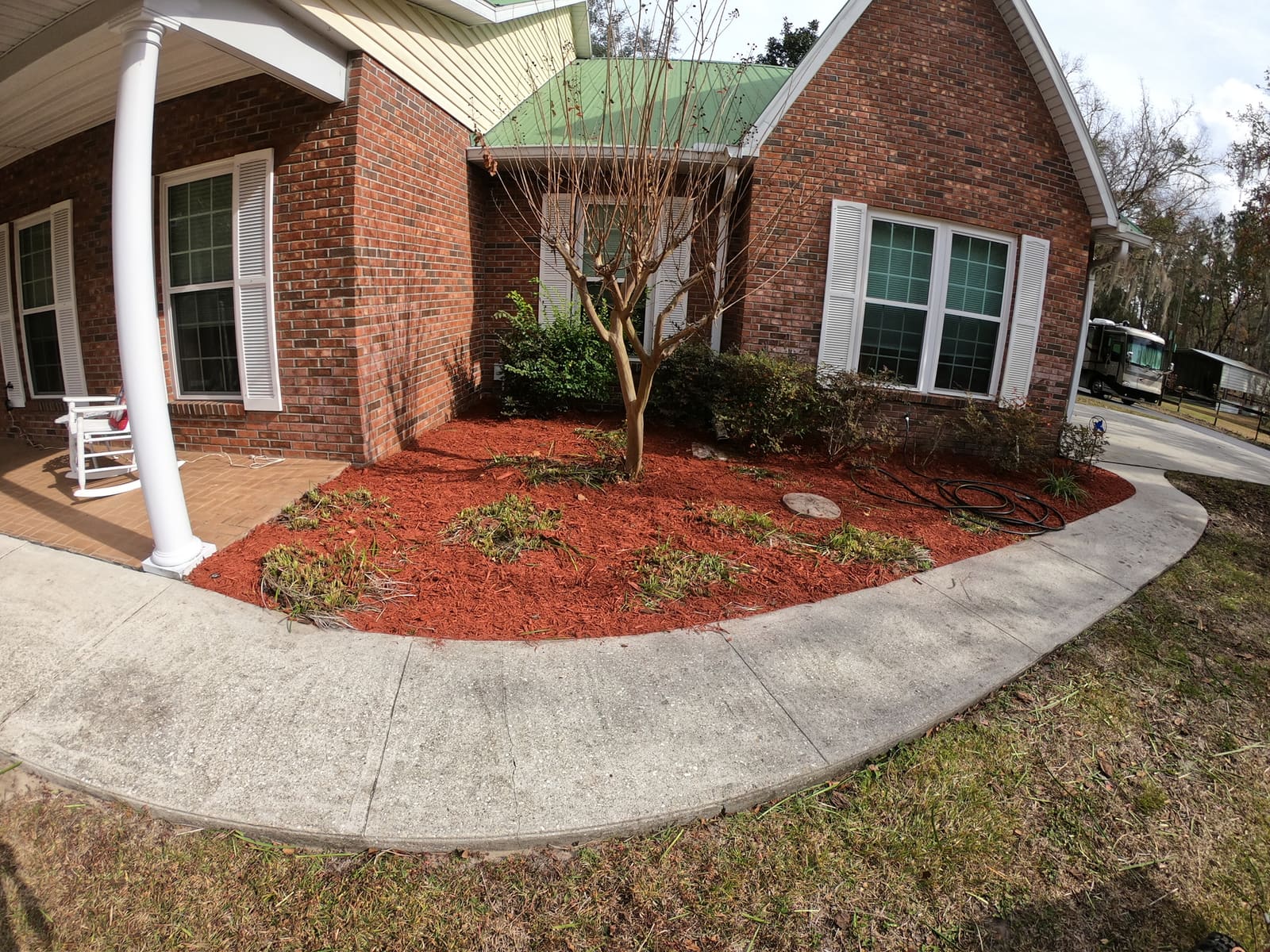 A mulch planting bed with a crape myrtle tree along a brick house