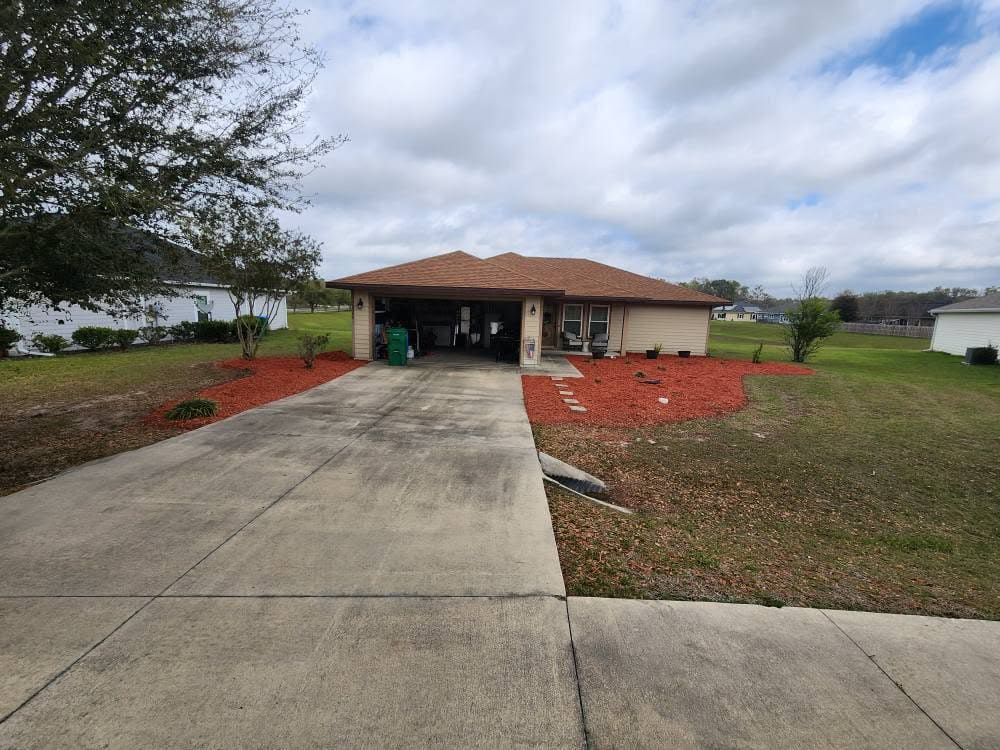 A mulch planting bed with potted plants in front of a house with an open garage