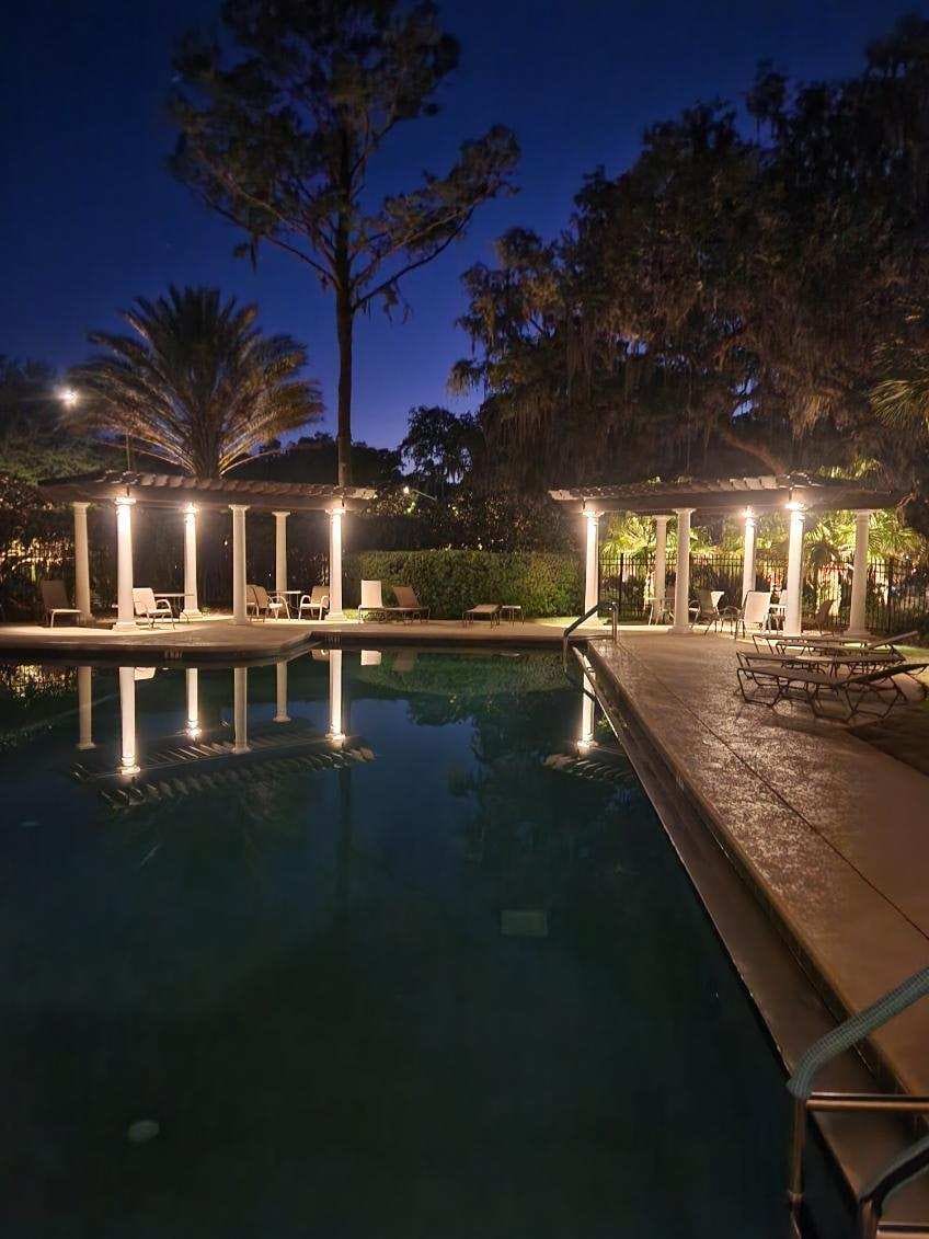A pool and pergola area lit with landscape lighting at night