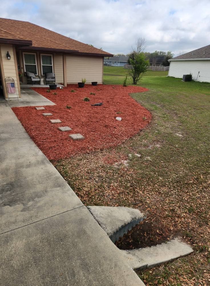 A red mulch bed with a drainage pipe extension in a front yard