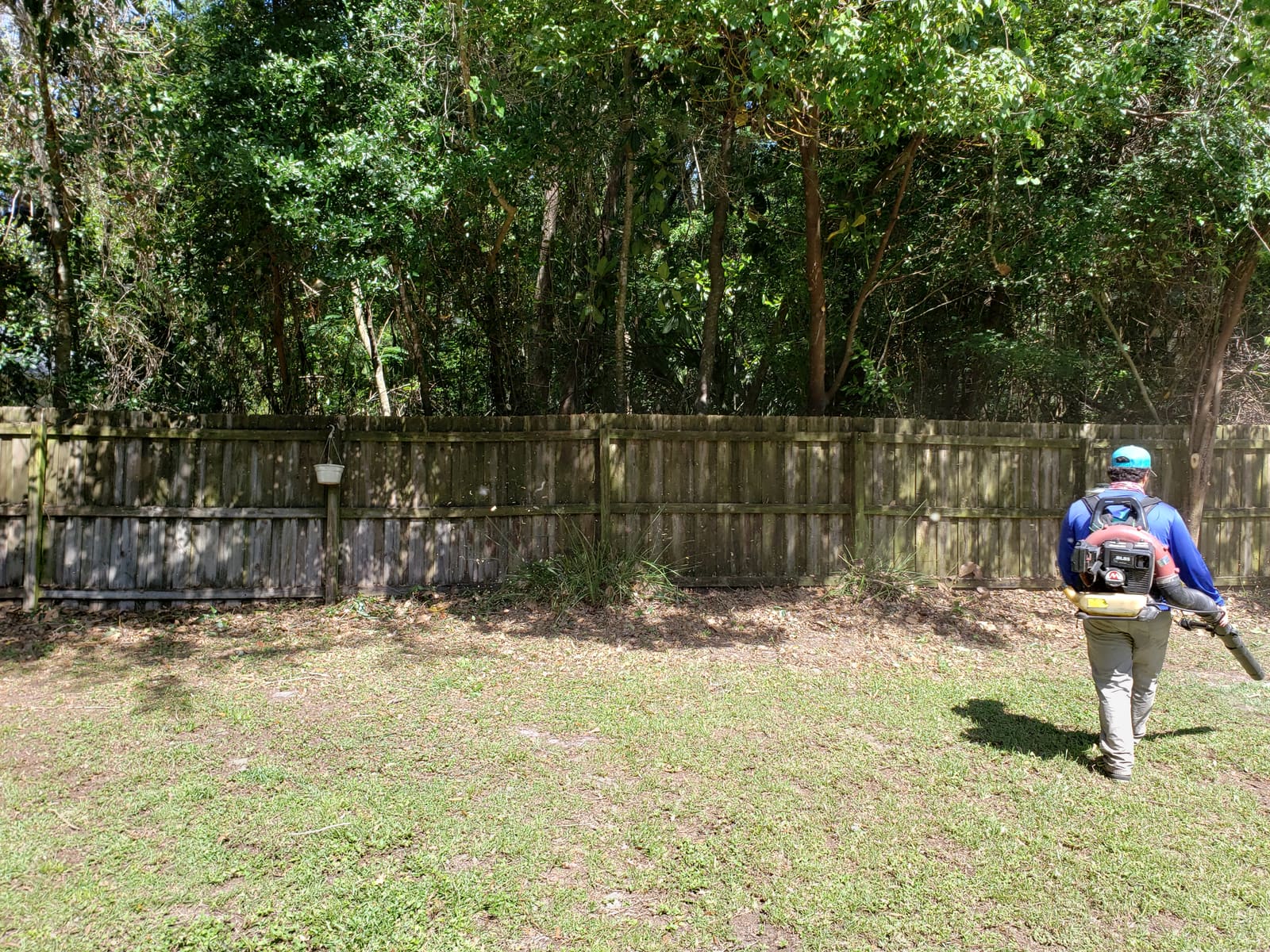 A crew member using a backpack blower to clear debris along a fence line