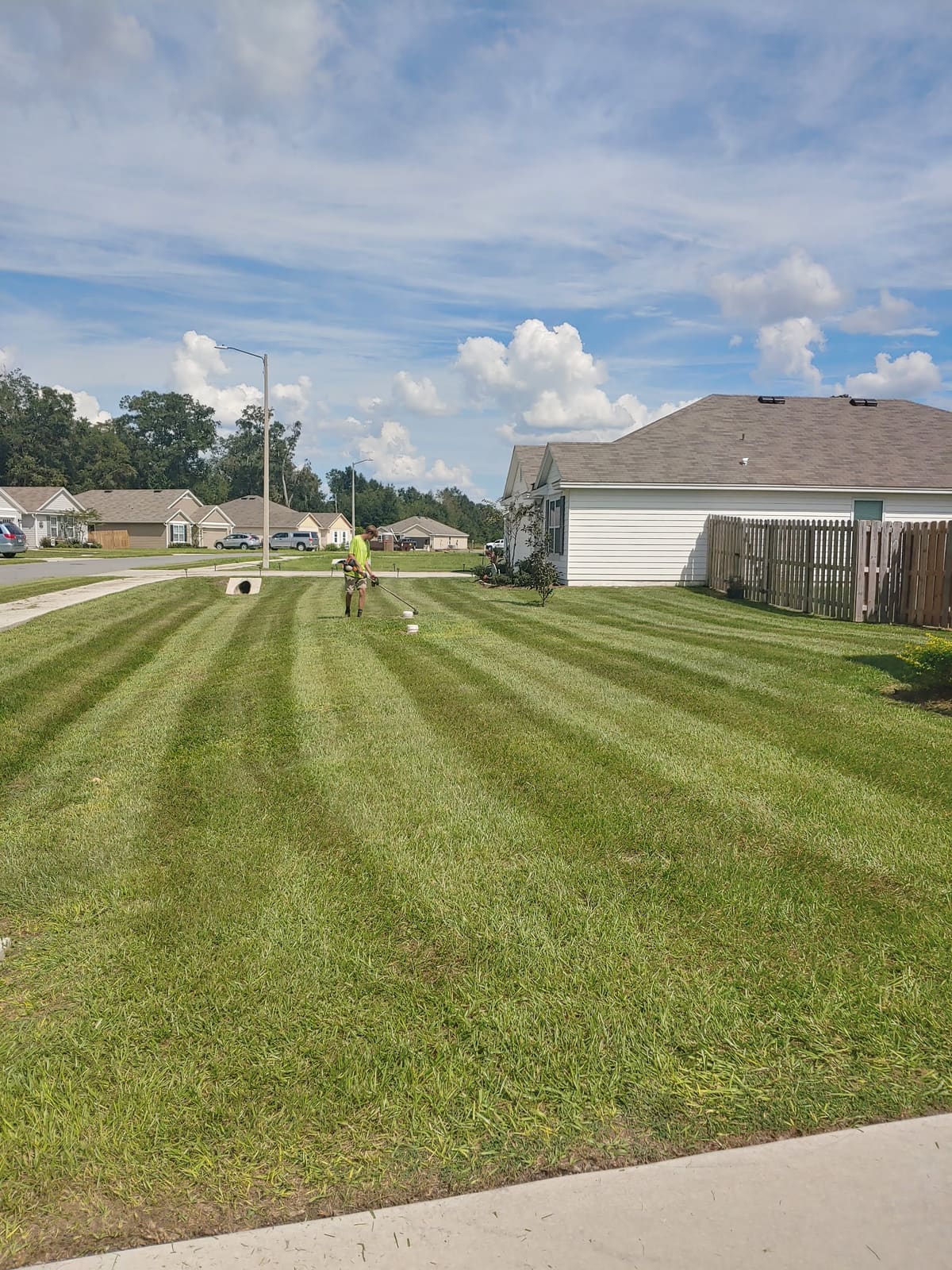 A striped, freshly mowed lawn with a crew member trimming in the background