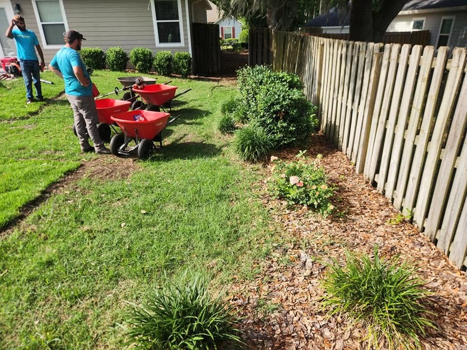 A crew clearing and treating a planting bed along a fence line