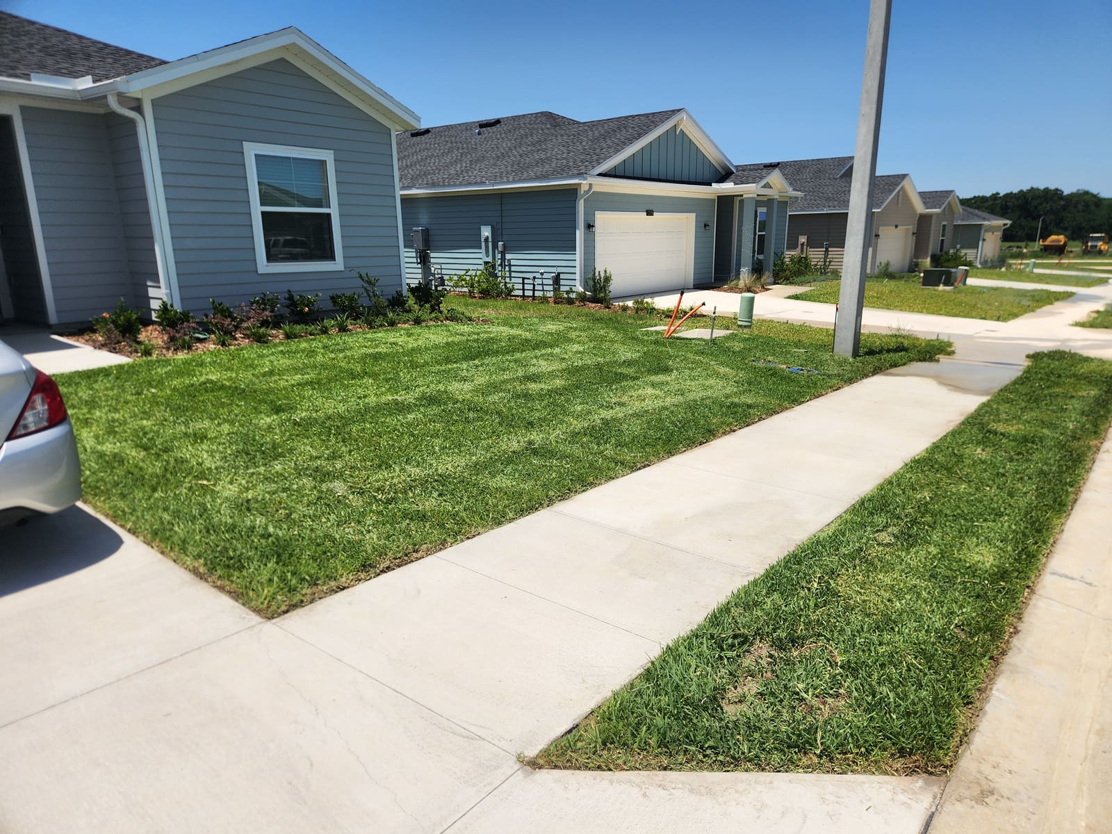 A striped, freshly mowed corner lawn beside a sidewalk