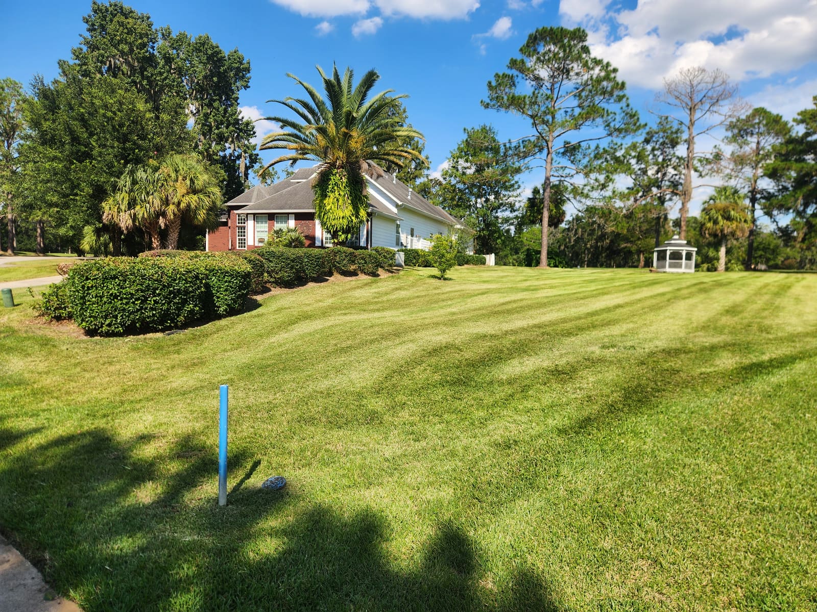 A striped, freshly mowed lawn beside a brick house and gazebo